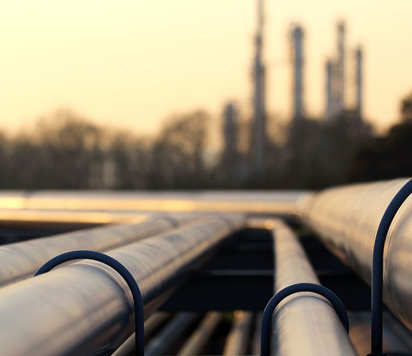 Rohrleitungsbau | Rohre stehen vor einer Raffinerie aufgereiht, bereit für den Einsatz in der industriellen Verarbeitung.
